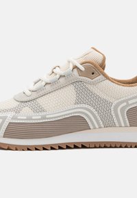 Sneaker sportivo con tomaia in rete beige e grigia, con intersuola testurizzata e suola in gomma per trazione. I lacci sono bianchi.