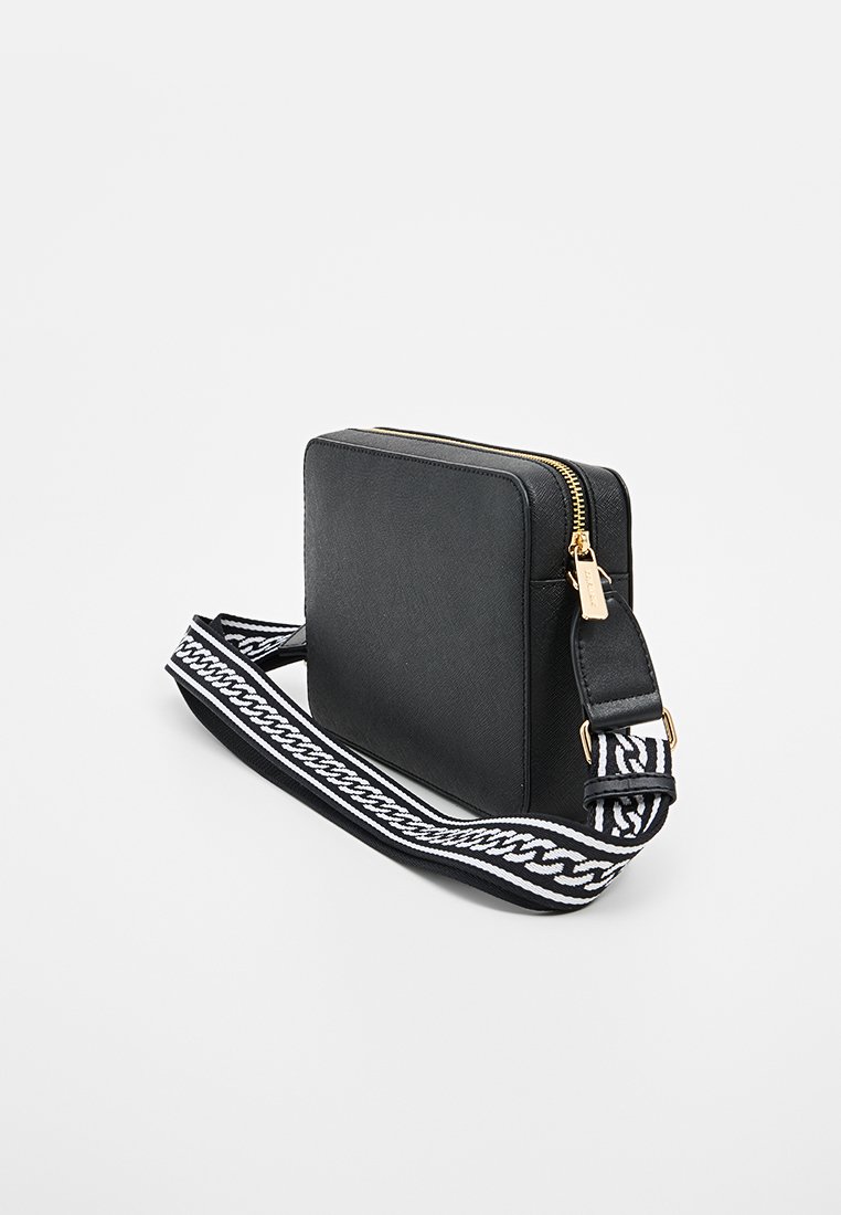 Czarna prostokątna torba na ramię z złotym zamkiem błyskawicznym i wzorzystym paskiem z białymi i czarnymi akcentami. Gładki materiał o teksturze.