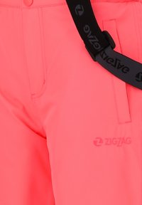 Pantalon rose vif avec des bretelles noires réglables et un logo ZIGZAG cousu près de la poche droite.