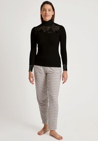 Zwart langemouwen top met kantdetail bij de hals en manchetten, gecombineerd met witte broek met een herhalend zwart golfpatroon.