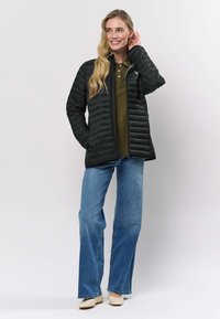 Svart dunjacka med quiltad struktur, frontblixtlås och sidofickor, bärs över en olivgrön pikétröja och ljusblå utsvängda jeans.