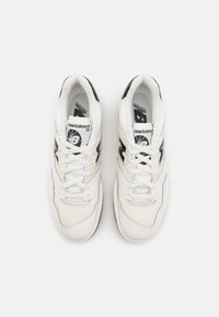 White leather sneakers with black accents, featuring a round toe, lace-up closure, and visible branding on the tongue and sides.