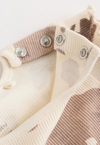 Gros plan sur un tissu côtelé beige et marron avec des boutons-pression métalliques sur un bord de vêtement plié.
