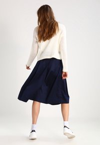 Lichte gebreide crèmekleurige trui gecombineerd met een vloeiende marineblauwe midi-rok. Witte sneakers met zwarte accenten maken de outfit compleet.