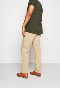 Pantaloni khaki con una vestibilità affusolata e tasche laterali, abbinati a una camicia a maniche corte verde scuro e scarpe eleganti marroni.
