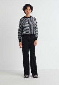 Maglione a righe bianche e nere in maglia, con maniche lunghe, scollatura rotonda e polsini a coste, abbinato a pantaloni neri a vita alta e scarpe con stampa zebra.