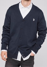 Mörkblå cardigan i stickad material med V-ringning, sex knappar, ribbade ärmslut och nederkant, samt en liten broderad logotyp på vänster bröst.