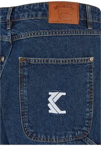 Temne modre jeans hlače z usnjenim oznakam blagovne znamke in izvezenim belim logotipom na zadnjem žepu. Imajo standardno šivanje in zakovice.