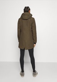 Brun, huvad parkas med en medellång design, texturerad tyg och en bakre ventilation. Bärs med svarta leggings och grå skor.