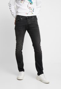 Jeans de mezclilla gris oscuro con corte slim, que cuentan con cinco bolsillos, un ligero desgaste y una textura desgastada. Combinados con zapatillas blancas.