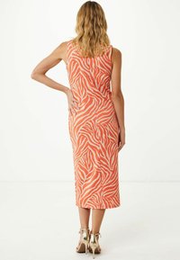 Abito midi arancione senza maniche con strisce bianche a zebra, stile aderente, tessuto morbido e spacco sul retro, abbinato a sandali con tacco alto dorati.