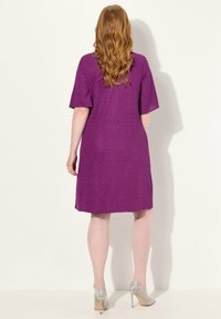 Robe courte à manches courtes, couleur violette, à coupe fluide, longueur genou, en tissu texturé, accompagnée de chaussures à talons hauts scintillantes de couleur argent.