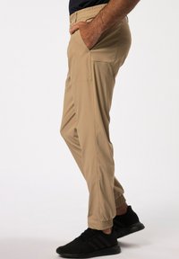 Pantalones cargo beige, ligeros, con cintura elástica, bolsillo lateral y puños ajustados, combinados con zapatillas deportivas negras.