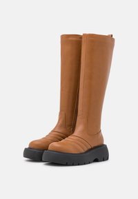 Bottes hautes jusqu'au genou en cuir fauve avec une fermeture éclair latérale, présentant des détails côtelés et une semelle en caoutchouc noir épaisse pour une meilleure adhérence et un confort accru.