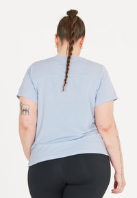 Ljust blå t-shirt med kort ärm, ribbad textur, rundad halsringning och lös passform, i kombination med svarta leggings.