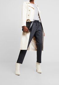 Kremowy płaszcz podwójnie zapięty z złotymi guzikami, szary sweter, ciemne spodnie w kratę oraz białe botki na wysokim obcasie. Czarna torebka z złotą rączką.