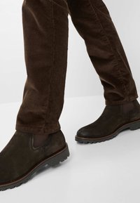 Braune Wildleder-Stiefeletten mit elastischen Seitenpaneelen und strukturierten Gummisohlen, getragen mit braunen Cordhosen, die ein glattes Finish präsentieren.