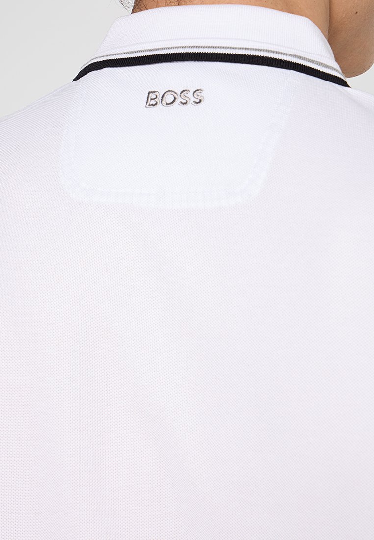 Camisa polo blanca con un tejido texturizado, un cuello a rayas en blanco y negro, y bordado plateado de "BOSS" en la parte posterior.