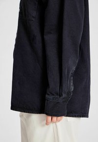 Dunkelblaue Jeanshemd mit lockerer Passform. Verfügt über einen Button-Down-Kragen, eine einzelne Brusttasche und umgeschlagene lange Ärmel. Glatte Textur.