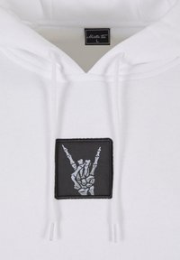 Hvid hættejakke med en sort lap, der har et grafisk motiv af en skelet hånd, der laver et 'rock on' tegn. Snører og blød tekstur.