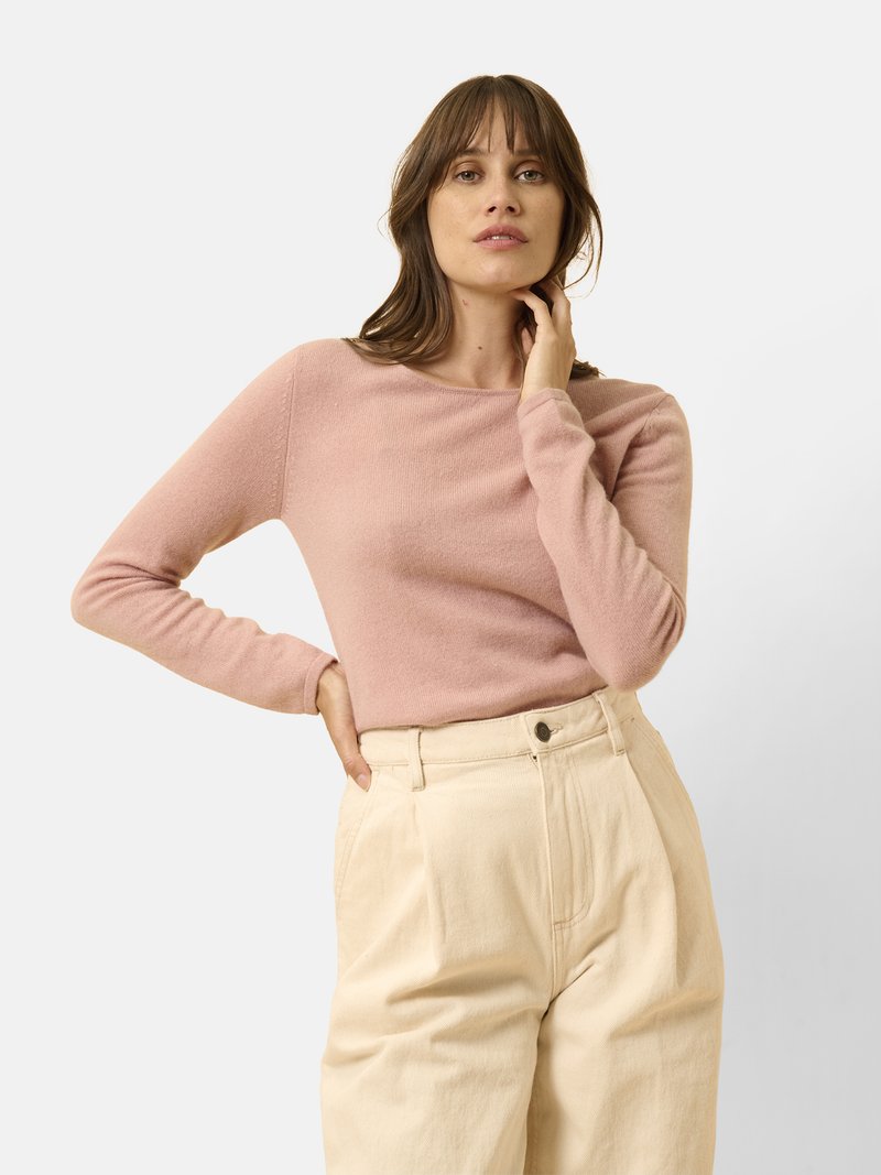Jasnoróżowy sweter z długim rękawem, wykonany z miękkiego materiału, zestawiony z spodnie szerokimi w kolorze kremowym z wysokim stanem. Prosty design, bez widocznych wzorów.