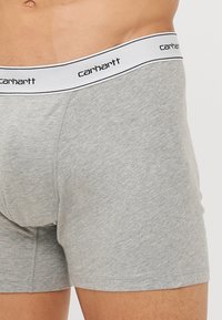 Boxeri din bumbac gri, cu un tiv alb pe care este imprimat logo-ul „Carhartt” în negru, cu o textură fină și un design ajustat.