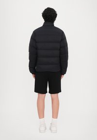 Puffetjakke i sort med høj krave og quiltet design. Sammen med sorte shorts og hvide sneakers, der viser en afslappet pasform.