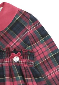 Un vestido a cuadros rojo y verde con cuello redondeado, cinturilla elástica y detalles con volantes, que presenta un pequeño lazo y un acento de botón.