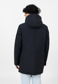 Schwarze Steppjacke mit hohem Kragen und Kapuze, ausgestattet mit einer glatten Textur, langen Ärmeln und einem lässigen Schnitt. Akzentuiert durch eine Seitentasche.