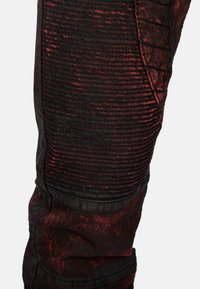 Jogger in denim nero e rosso scuro con effetto vissuto, texture a costine e dettagli trapuntati sui lati, caratterizzato da un design con gamba affusolata.