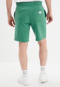 Pantalones cortos de algodón verde con un corte relajado, que cuentan con una cinturilla elástica, bolsillos y un bolsillo trasero cuadrado con una etiqueta.