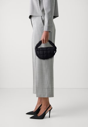 Black quilted handbag with a rounded handle, held in a hand. The outfit includes a checkered top and wide-leg pants, paired with black high heels.