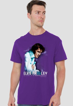 Man wearing purple t-shirt featuring Elvis Presley in white jumpsuit holding microphone with "Thirty Fifth Anniversary" text.