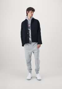 Chaqueta de algodón negra sobre una sudadera gris, combinada con joggers grises ligeros y zapatillas blancas. Texturas suaves; corte relajado.