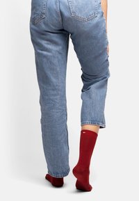 Calcetines de algodón rojos con una textura acanalada, usados con jeans de denim azul claro, con un detalle de logo en el puño, de altura al tobillo.