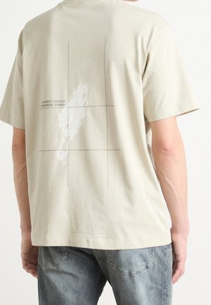 Hellbeiges Baumwoll-T-Shirt mit lockerer Passform. Auf der Rückseite befindet sich ein grafischer Druck mit Text und Gitterlinien, kurze Ärmel und ein Rundhalsausschnitt.