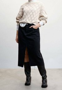 Jupe en jean noir avec une fente avant, associée à un pull en maille crème orné d'un motif en losange. Des bottes noires montant jusqu'aux genoux complètent ce look.