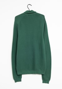 Grüner gerippter Pullover mit Kragen, langen Ärmeln und geradem Saum, der ein strukturiertes Strickmuster aufweist. Hängt an einem schwarzen Haken.