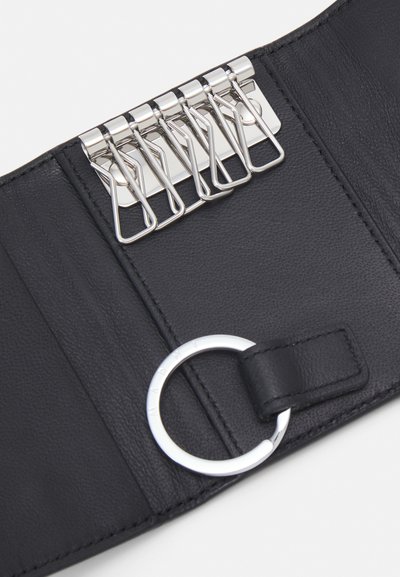 Portefeuille en cuir noir avec plusieurs clips métalliques, une finition texturée et un accent circulaire en argent avec une sangle en cuir.