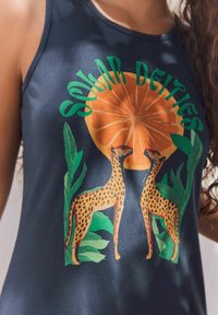 Top fără mâneci de culoare bleumarin cu un grafic portocaliu al soarelui și text verde "Zeii Solari." Prezintă leoparduri ilustrate cu pete galbene și foliaj.