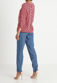 Blusa roja con estampado y mangas tres cuartos, combinada con pantalones azules sueltos y zapatos de tacón nude.
