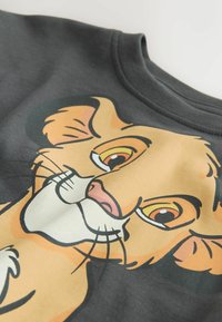 Sötétszürke pulóver, nagy oroszlánkölyök arcképével narancs és krémszínben, jellegzetes arcvonásokkal és kifejező szemekkel.