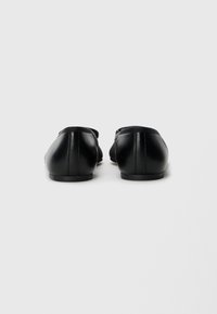Chaussures en cuir noir avec une semelle plate. L'arrière présente des lignes épurées et une texture lisse, avec un minimum de détails de couture.