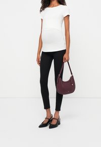 Camiseta de maternidad ajustada blanca, jeans ajustados negros, zapatos de tacón negros y un bolso de cuero burdeos con correa de hombro.