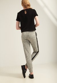 Sort tekstureret kortærmet top med detalje i nakken, parret med grå joggers med sorte side-striber og sorte snørebåndssko.