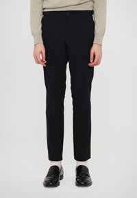 Marineblå bukser med en tætsiddende pasform, der har en glat overflade, standard talje og en enkelt knaplukning. Kombineret med sorte loafers.