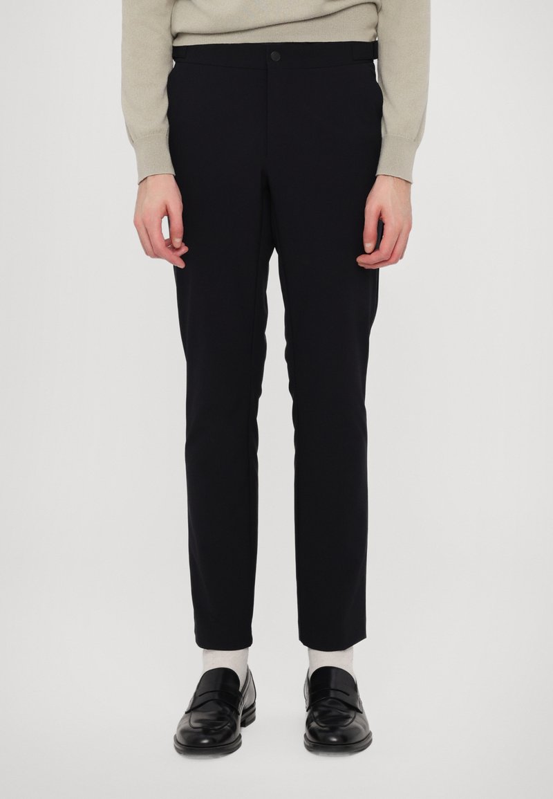 Marineblå bukser med en tætsiddende pasform, der har en glat overflade, standard talje og en enkelt knaplukning. Kombineret med sorte loafers.