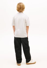 Ljusgrå t-shirt med korta ärmar och avslappnad passform; svarta baggyjeans med sidoficka; vita sneakers med ljusbruna sulor.