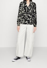 Svart omslagstopp med ett leopardmönster, långa ärmar och v-ringning, parat med krämfärgade vida cargobyxor och svarta sneakers.