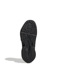 Suola di scarpa nera con motivi circolari e scanalature, vista dal basso, che proietta un'ombra su sfondo bianco.